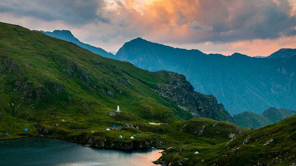 Do alto da montanha, vê-se barracas às margens do lago em um fim de tarde